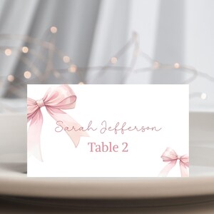 May include: White place card with a pink bow on the left and a smaller pink bow on the right. The text reads "Sarah Jefferson Table 2".
