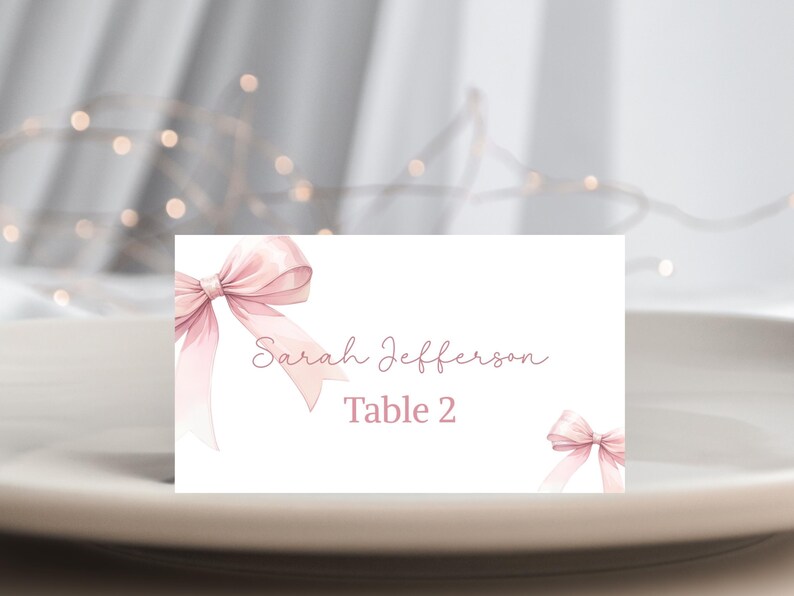 May include: White place card with a pink bow on the left and a smaller pink bow on the right. The text reads "Sarah Jefferson Table 2".