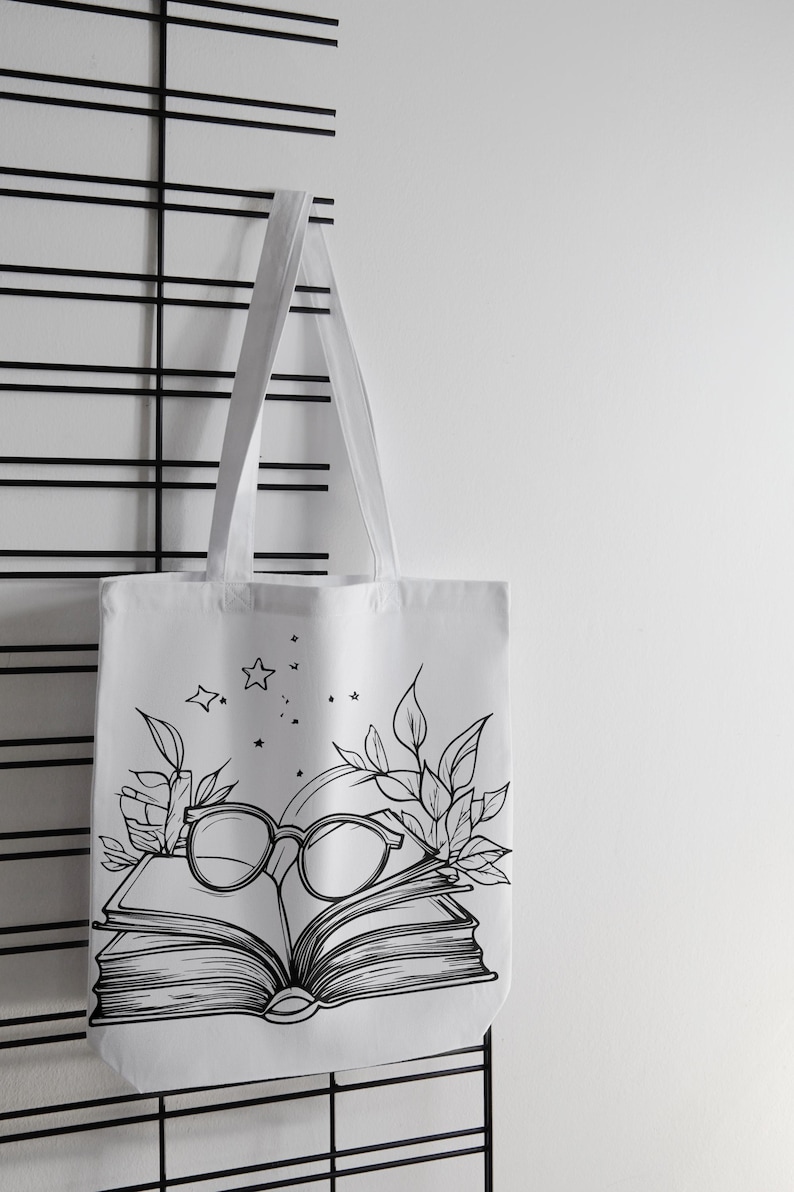 May include: White canvas tote bag with a black and white illustration of a book, glasses, and leaves. The illustration includes stars.