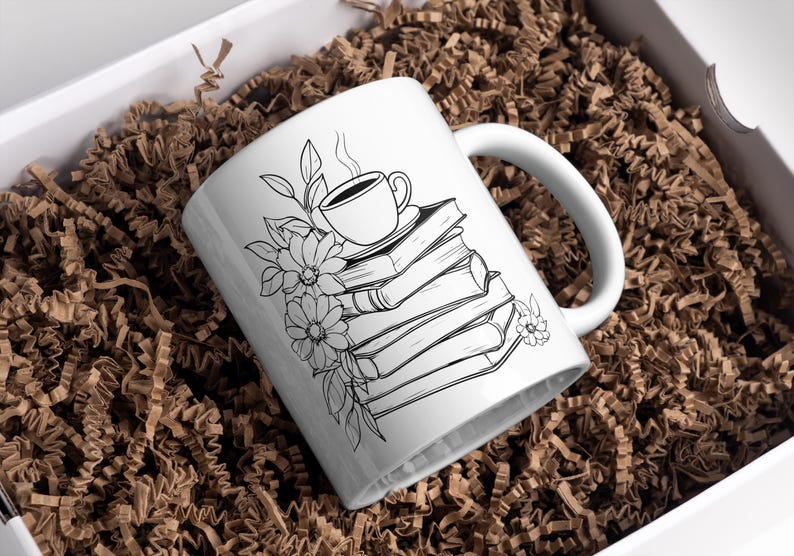 May include: White ceramic mug with a black line drawing of a cup of coffee on top of a stack of books with flowers around the base.