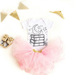 May include: A white baby onesie with a black and white illustration of a crescent moon and stars on top of a stack of books. The onesie is paired with a pink tulle tutu.