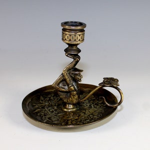 May include: A brass candlestick featuring a monkey holding a candle holder. The base is a circular tray with an intricate design.