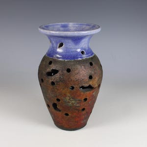 May include: A handcrafted ceramic vase with a blue top and a textured, brown body. The vase features numerous circular cutouts and a flared rim. The color transitions from blue to brown, creating a unique decorative piece.