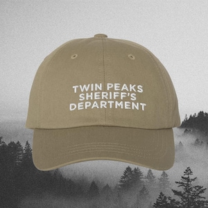 May include: A khaki baseball cap with white embroidered text that reads "Twin Peaks Sheriff's Department".