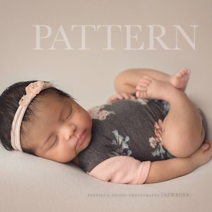 May include: A newborn baby girl sleeping on a white blanket, wearing a gray and floral patterned onesie with a pink trim and a pink headband with a flower accent. The baby is curled up with her arms and legs tucked in.
