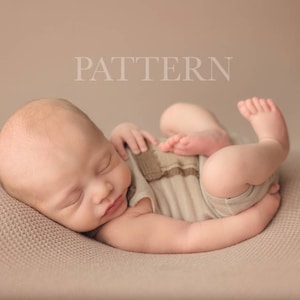May include: A newborn baby is sleeping on a light brown textured surface. The baby is wearing a light brown and white striped onesie.