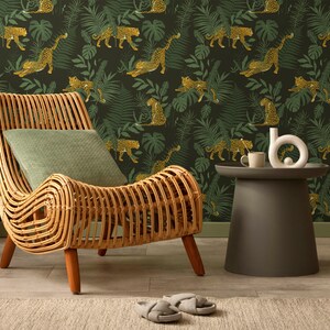 May include: A natural rattan armchair with a curved design and wooden legs. A green cushion rests on the chair. A small, dark grey side table holds a white vase and a mug. The background features a jungle-themed wallpaper with leopards and tropical leaves.