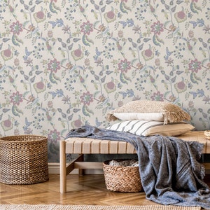 May include: A light beige wallpaper with a floral pattern featuring blue, green, pink, and yellow flowers. The wallpaper is shown in a room with a wooden bench, a wicker basket, and a throw blanket.