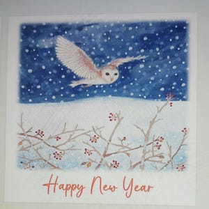 May include: A watercolour painting of a white barn owl flying through a snowy night sky. The owl has a brown and white pattern on its wings. The sky is blue with white dots representing snow. The text "Happy New Year" is written in orange at the bottom of the image.