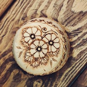 May include: A wooden bowl with a carved floral design. The bowl is light brown and the flowers are white with dark centers.