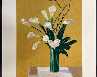 Pode incluir: Um arranjo de flores de lírio branco em um vaso verde sobre uma toalha de mesa branca. As flores estão dispostas em um vaso sobre uma mesa com um fundo dourado.