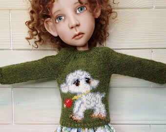 Può includere: Una bambola con i capelli rossi ricci che indossa un maglione verde con un disegno di agnello bianco, una gonna floreale blu e bianca, collant bianchi e scarpe bianche con orecchie di coniglio. La bambola tiene un agnello di peluche bianco con gli occhi blu.