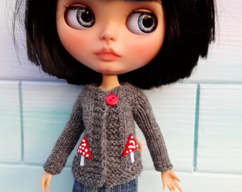 May include: A doll with black hair and blue eyes wearing a gray knitted cardigan with mushroom embroidery. The cardigan has a red button.