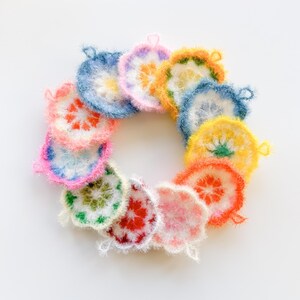 May include: A set of 14 colorful crocheted dishcloths in a variety of floral patterns. The dishcloths are arranged in a circle, with the colors ranging from pink to yellow to blue.