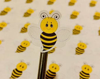 May include: A sheet of white paper with multiple yellow and black bee stickers. One bee sticker is on a silver pencil.