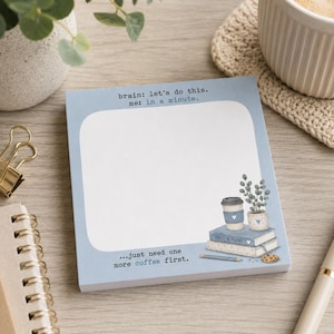 Könnte beinhalten: Ein quadratischer Notizblock mit hellblauem Rand und weißer Mitte. Der obere Text lautet "brain: let's do this. me: in a minute." Der untere Text lautet "...just need one more coffee first." Eine Illustration zeigt Bücher, eine Kaffeetasse und eine Pflanze.
