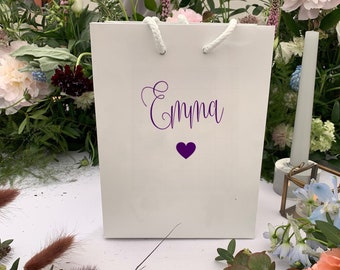 May include: White gift bag with a purple heart and the name "Emma" written in cursive.