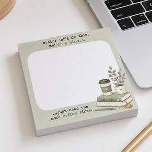 Peut inclure: Un bloc-notes carré avec une bordure vert sauge et un centre blanc. Le texte en haut indique, Brain: let's do this. me: in a minute. Le texte en bas indique, ...just need one more coffee first. Une illustration montre un café, des livres et une plante.