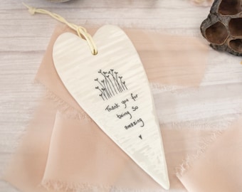 May include: A heart-shaped ceramic ornament with a cream-coloured, textured surface. It features a black line drawing of small flowers and the handwritten text, "Thank you for being so amazing," with a small heart symbol. A light-coloured string is attached.