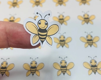 May include: A small die-cut sticker featuring a cartoon bee with yellow wings, a black and yellow striped body, and two antennae. The bee has a smiling face with large eyes. The sticker is shown against a sheet of identical bee stickers.