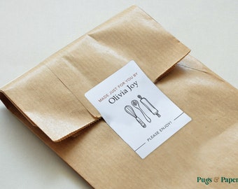 May include: A brown paper package with a white label that reads "MADE JUST FOR YOU BY Olivia Joy" with illustrations of a whisk, spoon, and rolling pin. The text "PLEASE ENJOY!" is also on the label.