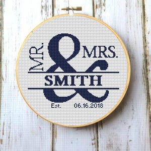 May include: A white embroidery hoop with a navy blue ampersand symbol and the text "Mr. & Mrs. Smith Est. 06.16.2018".