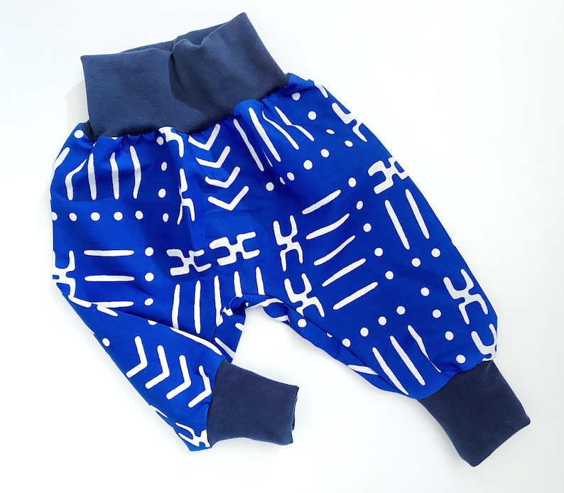 May include: Blue and white patterned baby pants with navy blue cuffs. The pants have a geometric pattern.