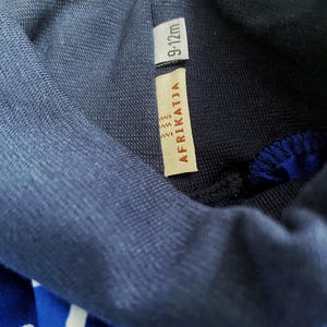 May include: A navy blue turtleneck sweater with a white and blue patterned design. The sweater has a tag that says "AFRIKATJIA" and "9-12m".