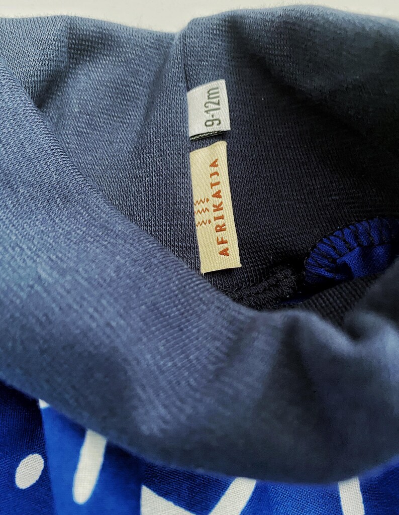 May include: A navy blue turtleneck sweater with a white and blue patterned design. The sweater has a tag that says "AFRIKATJIA" and "9-12m".