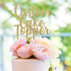 May include: Gold glitter cake topper with the text "Custom Cake Topper" on a white cake with pink roses.