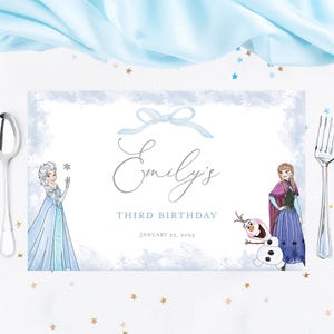 May include: A personalized birthday placemat with a light blue watercolor design. The placemat features the name "Emily's" in cursive, the text "THIRD BIRTHDAY", and the date "JANUARY 25, 2025". Elsa, Anna, and Olaf are illustrated on the placemat.