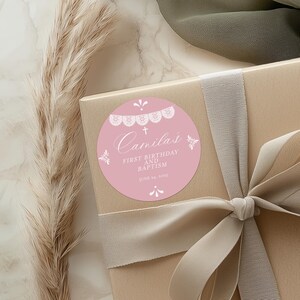 May include: Pink and white round sticker with a lace design and the text "Camila's First Birthday and Baptism June 24, 2023".