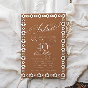 May include: A rectangular invitation card with a brown background and a white floral border. The card reads "Salud!" and invites guests to Natalie's 40th birthday celebration. Details include the date, time, and location.