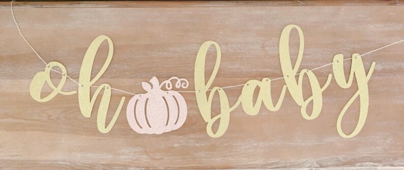 May include: A gold glitter banner with the text "oh baby" and a pink glitter pumpkin in the middle.
