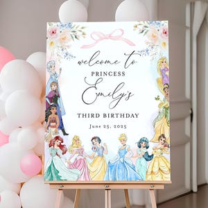 以下が含まれることがあります： プリンセスをテーマにした3歳の誕生日パーティーのウェルカムサイン。サインには、ディズニーのプリンセスのイラスト、花の装飾、そして「Welcome to Princess Emily's Third Birthday June 25, 2025」というテキストが描かれています。
