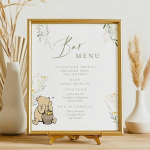 May include: A framed bar menu with a gold border, featuring a floral design and the words "Bar Menu." The menu lists signature drinks, beer, cocktails, and non-alcoholic options. A Winnie the Pooh graphic is on the bottom left.