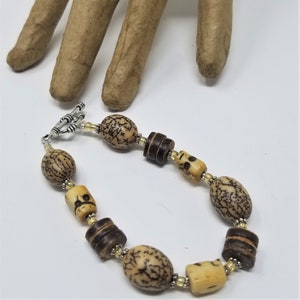 May include: A brown and beige bracelet with a silver clasp. The bracelet is made of wooden beads and seed pods.