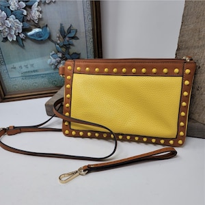 May include: A yellow leather crossbody bag with brown trim and gold studs. The bag has a long adjustable strap and a shorter handle.