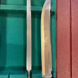Pu&ograve; includere: Primo piano di due coltelli da cucina argentati con manici neri. Il coltello a sinistra &egrave; un acciaio per affilare e il coltello a destra &egrave; un coltello da intaglio. Il coltello da intaglio ha la scritta "Stainless Steel U.S.A." incisa sulla lama.