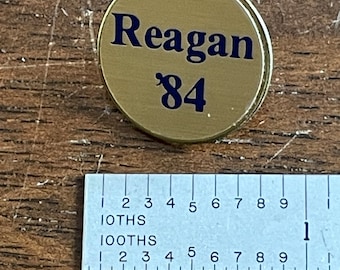 Vintage 1980 “Reagan ‘84“ button in gold with blue writing.