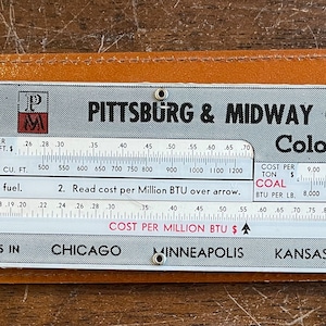 May include: A vintage metal slide rule for calculating the cost per million BTUs of oil, gas, and coal. The slide rule is labeled "Pittsburg & Midway Coal Co. Colonial Coal" and has scales for BTU values, cost per gallon, cost per cubic foot, and cost per ton. The slide rule is in a brown leather case.