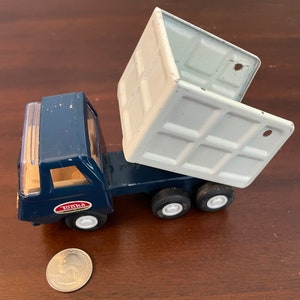 May include: A blue Tonka toy dump truck with a white metal bed. The bed is raised and the truck has four black wheels.