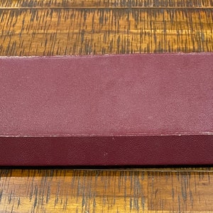 Pu&ograve; includere: Una scatola rettangolare di colore bordeaux con bordi arrotondati. La scatola ha due piccoli bottoni rotondi di colore rosso scuro sul davanti.
