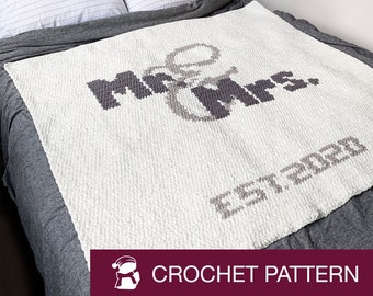 Op de afbeelding: Wit gebreid deken met de woorden "Mr & Mrs. Est. 2020" in grijs garen.