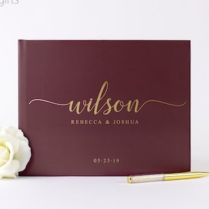 May include: Burgundy guest book with gold lettering. The book says "wilson" in cursive, "Rebecca & Joshua" and "05-25-19".