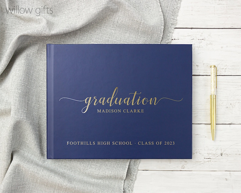 May include: A navy blue graduation guest book with gold lettering. The book says "graduation" with the name "MADISON CLARKE" underneath. It also says "FOOTHILLS HIGH SCHOOL - CLASS OF 2023".