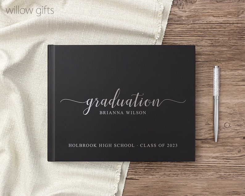 May include: Black graduation guest book with silver lettering. The book says "graduation" with the name "Brianna Wilson" and "Holbrook High School - Class of 2023".
