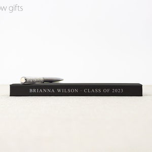 May include: A black gift box with a silver pen on top. The box has the text "BRIANNA WILSON - CLASS OF 2023" printed on it.