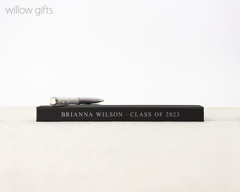 May include: A black gift box with a silver pen on top. The box has the text "BRIANNA WILSON - CLASS OF 2023" printed on it.