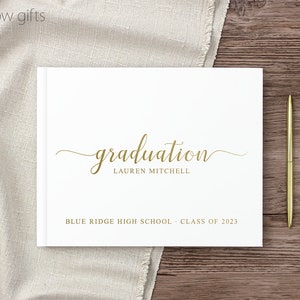 May include: White graduation guest book with gold lettering. The book says "graduation" with the name "Lauren Mitchell" below. The book also says "Blue Ridge High School - Class of 2023".
